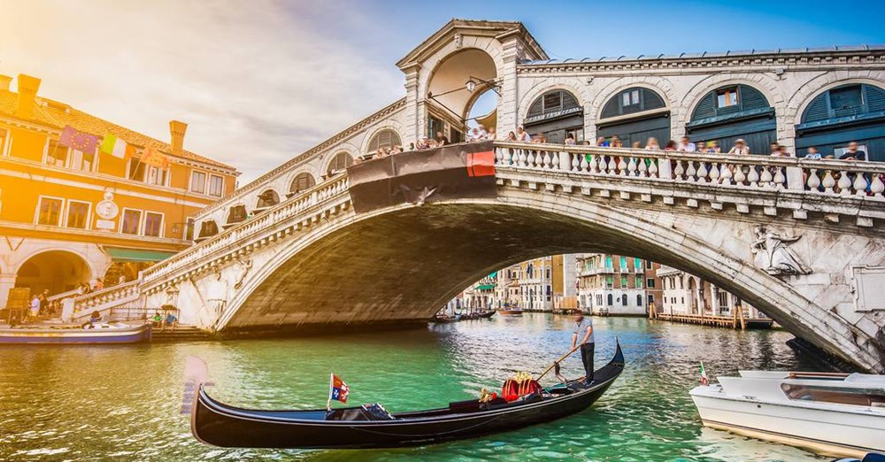 En gondol nærmer sig Rialto-broen på Canal Grande i Venedig, Italien på en solrig dag med mennesker, der går over broen.