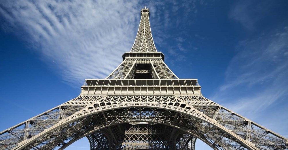Eiffeltårnet dominerer landskabet mod en klar blå himmel prydet med spredte stribeformede skyer.