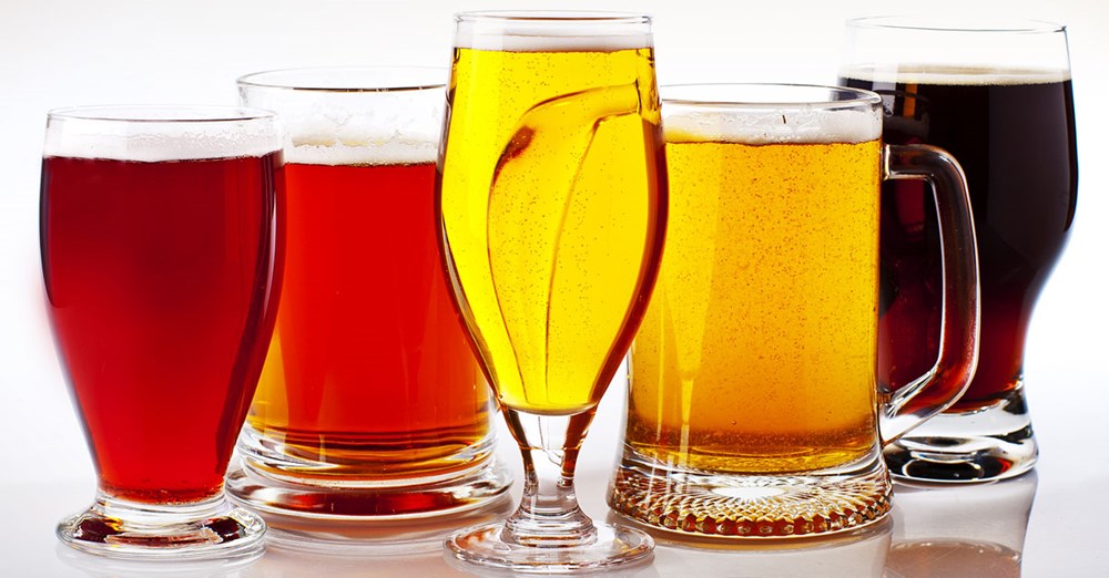 Fire forskellige glas fyldt med øl i varierende farver og skum fra lys gylden til dyb mørkebrun.