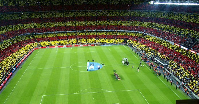 Fyldt fodboldstadion på Camp Nou, med en farverig menneskemængde, der er klar til at overvære en fodboldkamp på en grøn fodboldbane.