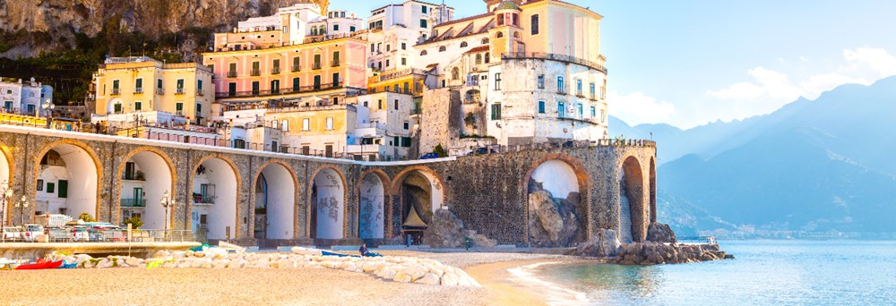 Amalfi med farverige bygninger på klipperne og en buegang, der når ud til det azurblå hav.