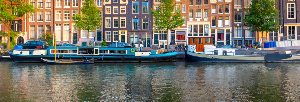 Farverige huse langs en kanal med parkerede både på en solrig dag i Amsterdam.
