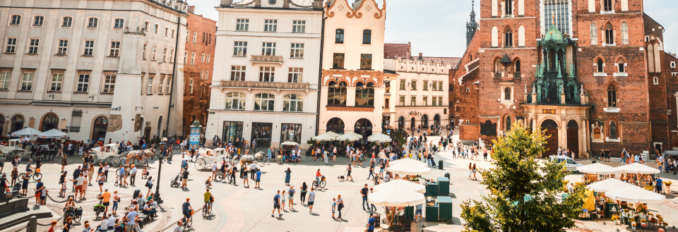 Den centrale Rynek plads i Krakow, der går rundt og nyder solskinnet, omgivet af historiske bygninger og udendørs caféer.