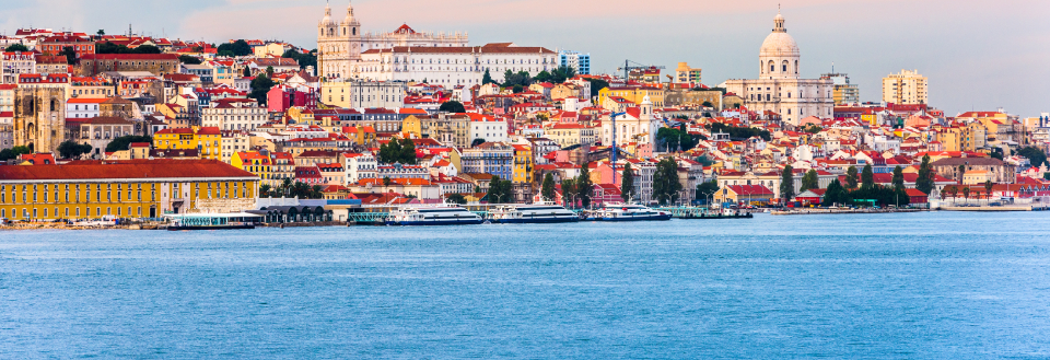 Lissabons vandkant i den gyldne time med historiske bygninger og dominerende kirketårne.