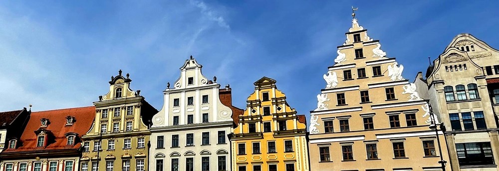Farverige bygninger på Rynek-pladsen i Wroclaw med klassisk europæisk arkitektur og dekorative gavle under en blå himmel.