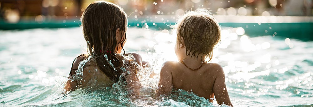 To børn leger i en pool med lyset fra solnedgangen glitrende på vandoverfladen omkring dem.
